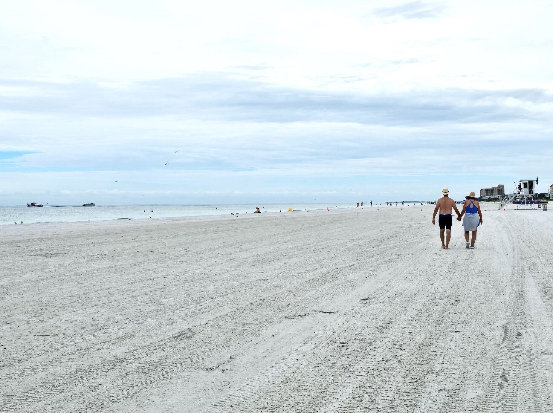 A wide sandy beach with a lifeguard tower and a pier in the distance.