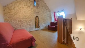 Une chambre à coucher confortable, aménagée dans un grenier avec un plafond en pente, un mur en pierre, un escalier en bois et un canapé rouge.