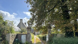 Un chemin de gravier mène à un portail en pierre, avec une église en arrière-plan.