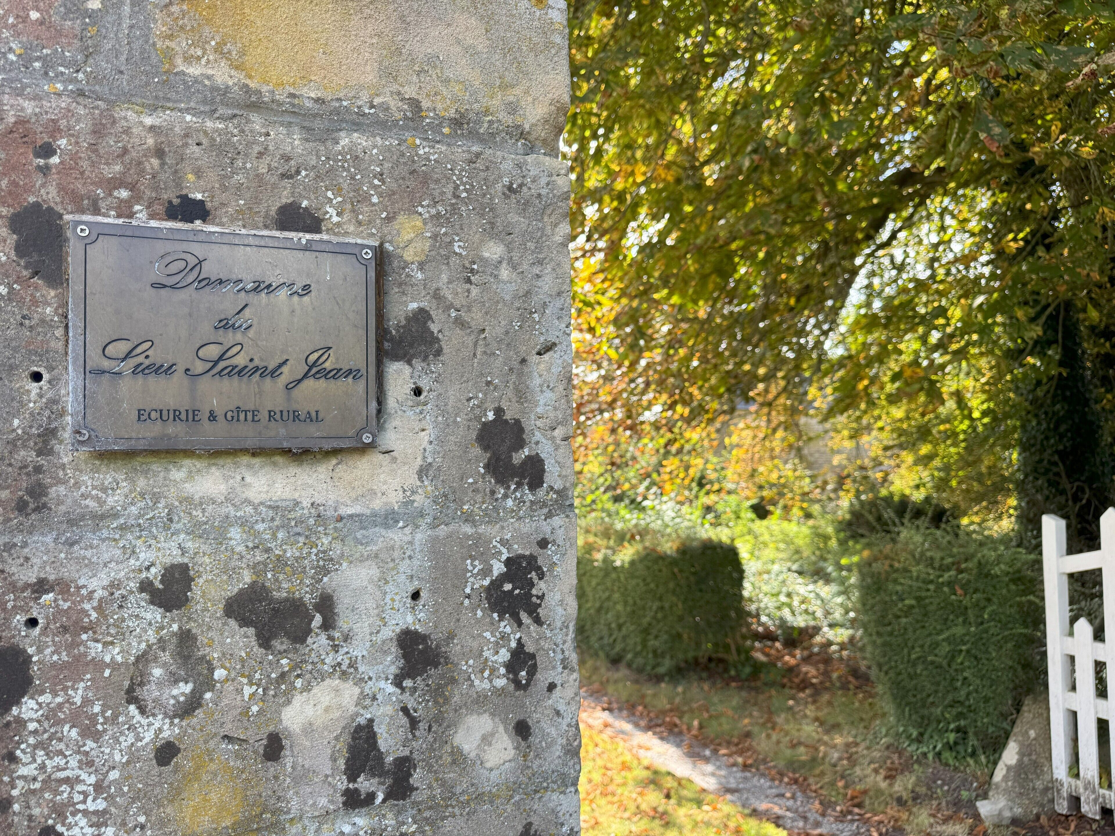 A weathered sign on a stone wall with the inscription "Domaine des Lieu Saint Jean ECURIE & GÎTE RURAL."