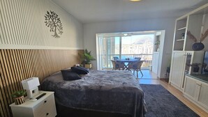 Une chambre à coucher avec un lit, une table de chevet et une vue sur la ville grâce à de grandes fenêtres.