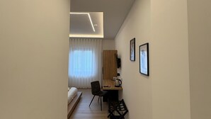 A narrow hallway leading to a bedroom with a bed, a desk, and a chair. - Domus Matronae (Castellammare di Stabia)