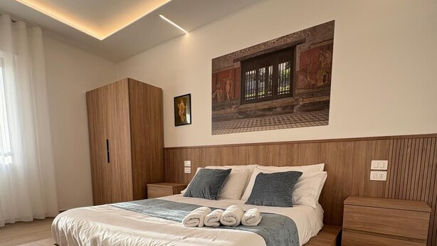 A modern bedroom with a large bed, wooden headboard, and a wall-mounted artwork. - Domus Matronae (Castellammare di Stabia)
