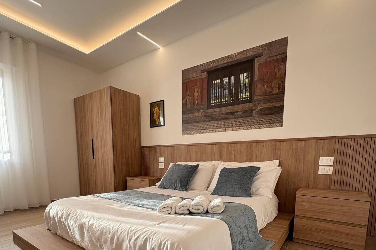 A modern bedroom with a large bed, wooden headboard, and a wall-mounted artwork.