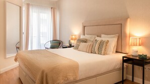 Une chambre à coucher avec un grand lit, deux tables de chevet avec des lampes, une chaise et une fenêtre avec des rideaux.