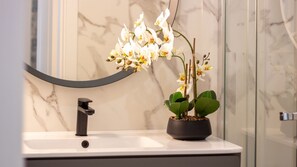 Ein Badezimmer mit Marmorwaschbecken, einem modernen Wasserhahn und einer Orchidee im Topf.