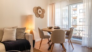 Ein modernes Wohnzimmer mit einer Couch, einem Tisch mit Stühlen, einer Lampe und Blick auf den Balkon.