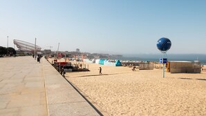Une plage avec un ciel dégagé, une grande structure sphérique bleue et des gens qui se promènent.