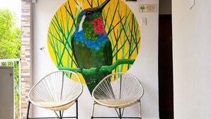 A room with a wooden ceiling, two wicker chairs, a colorful mural of a hummingbird, and a white wall. - Selva Maria Tayrona  (Santa Marta)