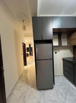 Une cuisine moderne avec des meubles de couleur sombre, un réfrigérateur à deux portes et un sol en marbre.