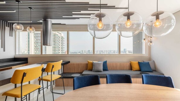 A modern office space with a large round table, yellow chairs, a sofa with blue and gray cushions, and a city view through large windows. - Apartment with 1 parking space - near the US Consulate! (Vila Sao Francisco (Zona Sul) São Paulo)