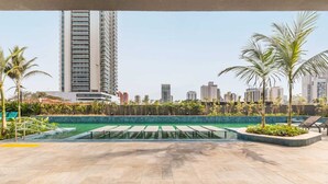 A rooftop pool area with lounge chairs, palm trees, and a cityscape in the background. - Apartment with 1 parking space - near the US Consulate! (Vila Sao Francisco (Zona Sul) São Paulo)