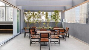 A rooftop terrace with a long table and chairs, surrounded by potted plants, and large windows offering a city view. - Apartment with 1 parking space - near the US Consulate! (Vila Sao Francisco (Zona Sul) São Paulo)