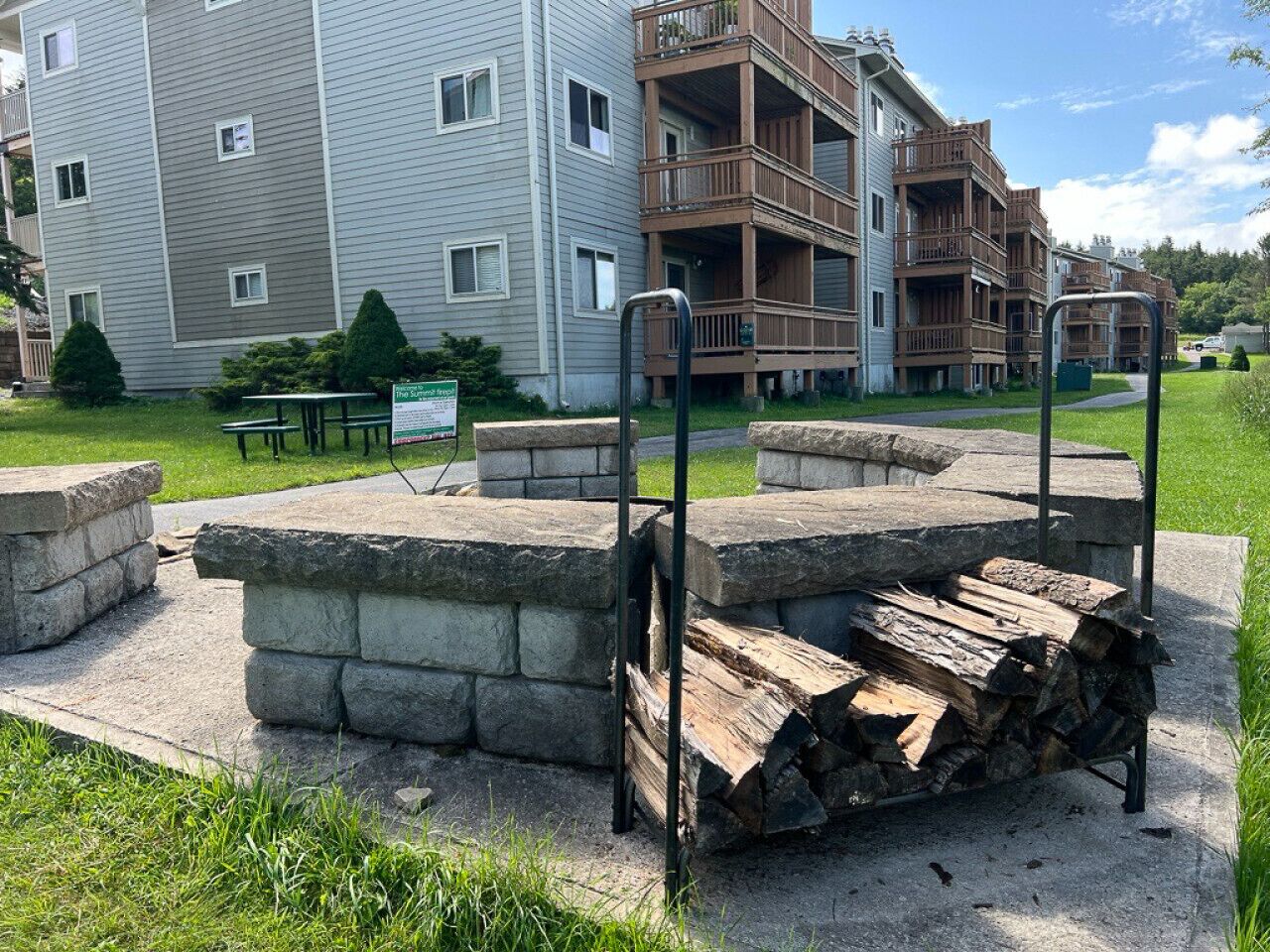 A stone fire pit with a metal stand in a courtyard with apartment buildings in the background.