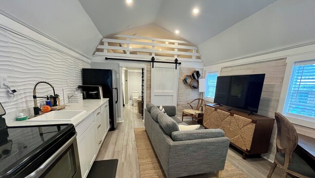 A compact living space with a kitchenette, a gray sofa, a TV, and a dining area. - Tiny house monthly rental with small office in central North Charleston with AC (North Charleston)