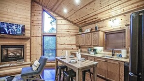 A cozy cabin interior with a wooden interior, a fireplace, a dining area, and a kitchen with wooden cabinets.