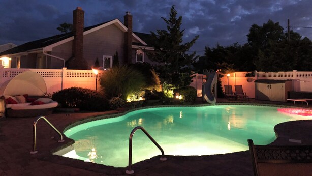Una piscina con una escalera de metal, una silla de descanso y una zona de estar cubierta.