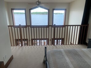 A room with a balcony overlooking a body of water, a ceiling fan, and a bed with a patterned bedspread.