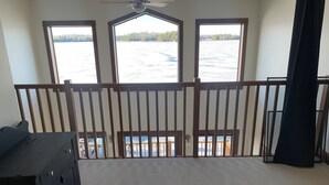 Quarto com varanda com vista para um lago, ventilador de teto e cômoda preta.