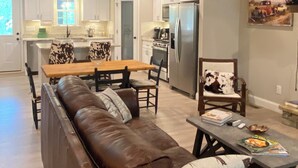 Amplia sala de estar con sofá de cuero, mesa de comedor de madera y cocina al fondo.