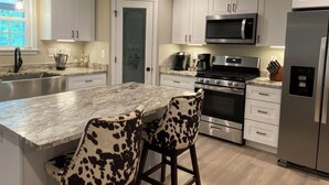 Una cocina moderna con armarios blancos, un refrigerador de acero inoxidable, un microondas y una estufa a gas. Hay dos taburetes de bar con diseño de vaca.