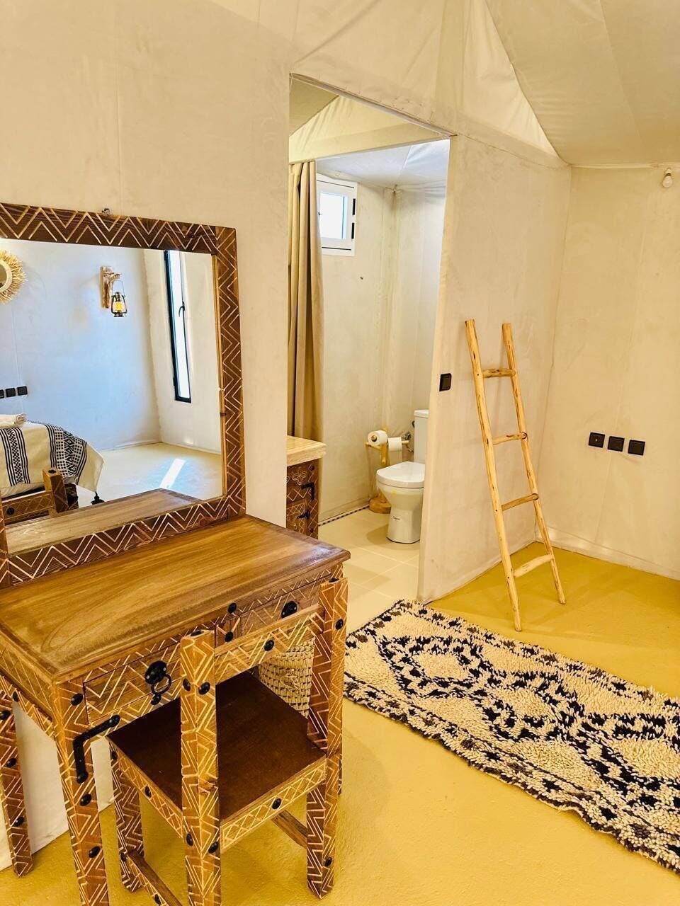 Ein Zimmer mit einem Holztisch, einem Spiegel, einem gemusterten Teppich, einer Hartsreppe und Blick ins Badezimmer.