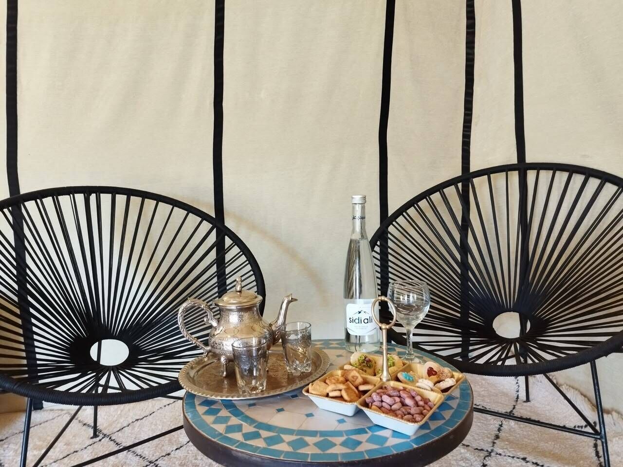 Une table dressée avec une théière, des verres, une bouteille et un plateau de collations.