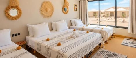 Una camera d'albergo con tre letti, un'ampia finestra e vista sul deserto.