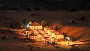 Un resort en el desierto con varias tiendas de campaña y un edificio central, rodeado de dunas de arena.