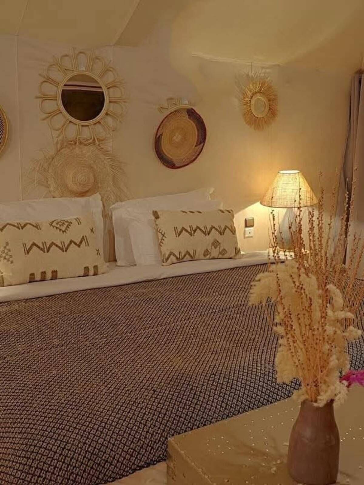 A room with a bed, decorative wall mirrors, a lamp, and a vase with dried plants.