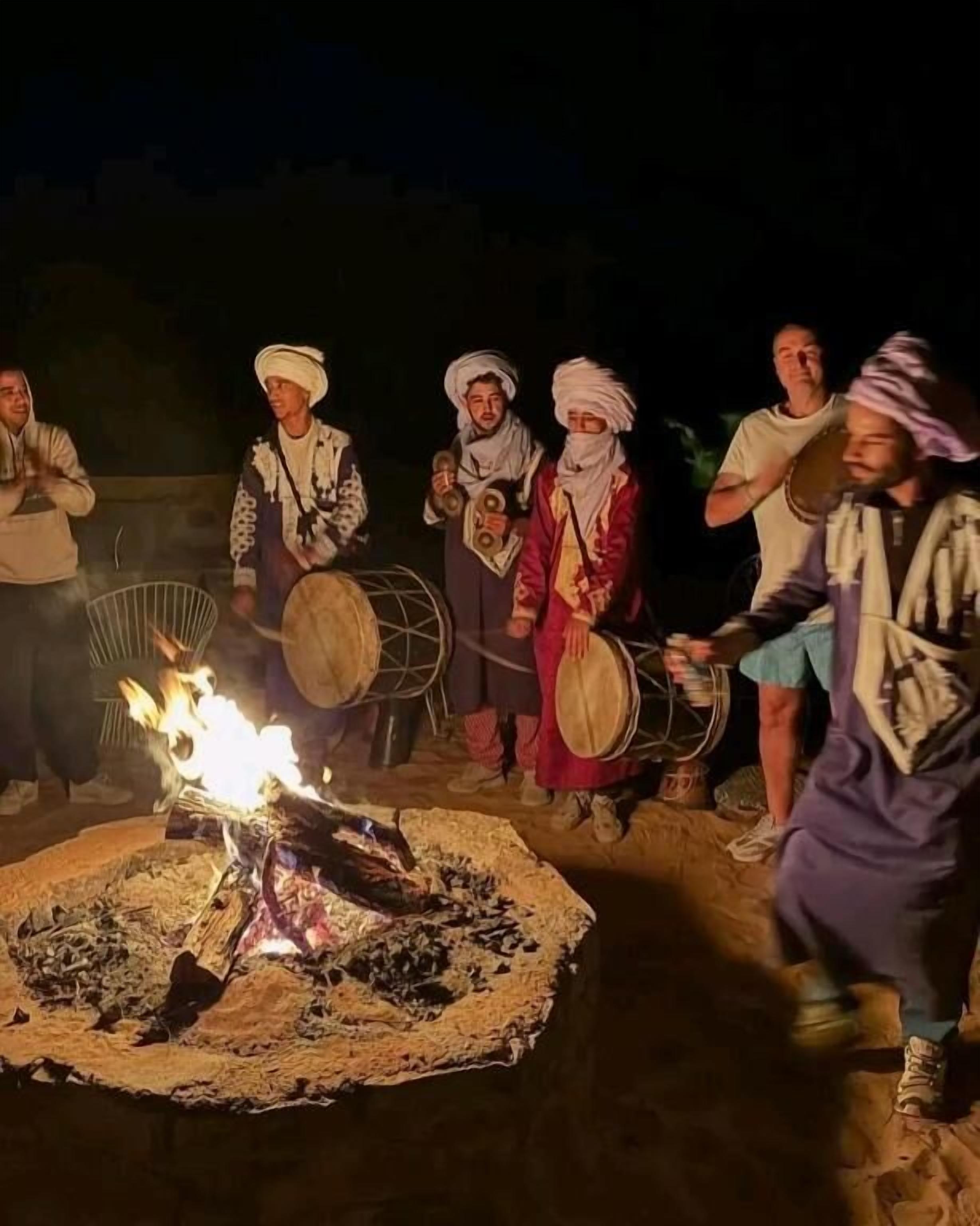 A group of people playing traditional drums around a campfire at night.