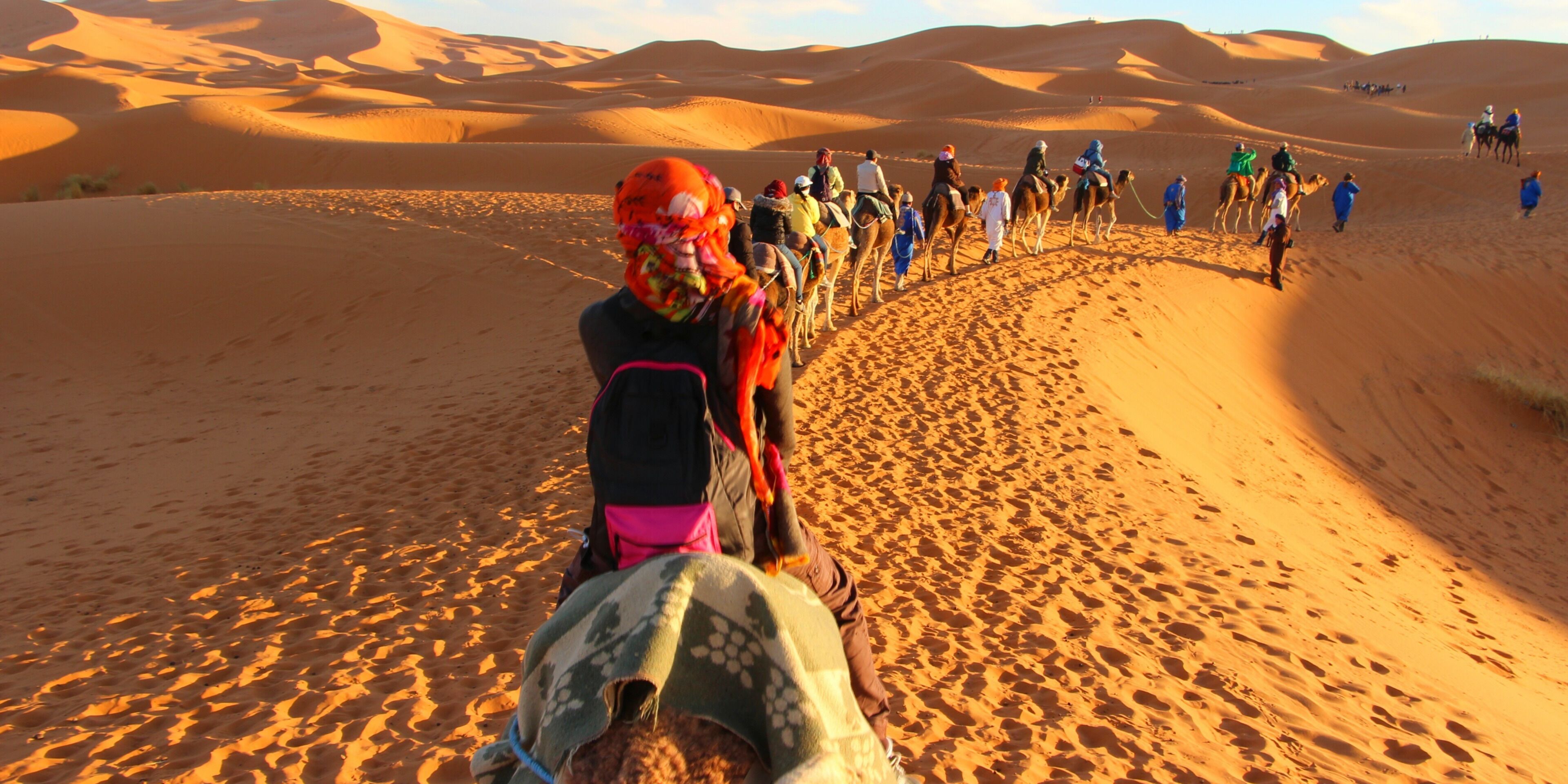 A group of people riding camels through a desert landscape with sand dunes.