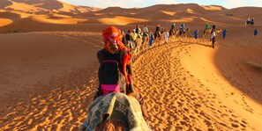 Un grupo de personas montando camellos a través de un paisaje desértico con dunas de arena.