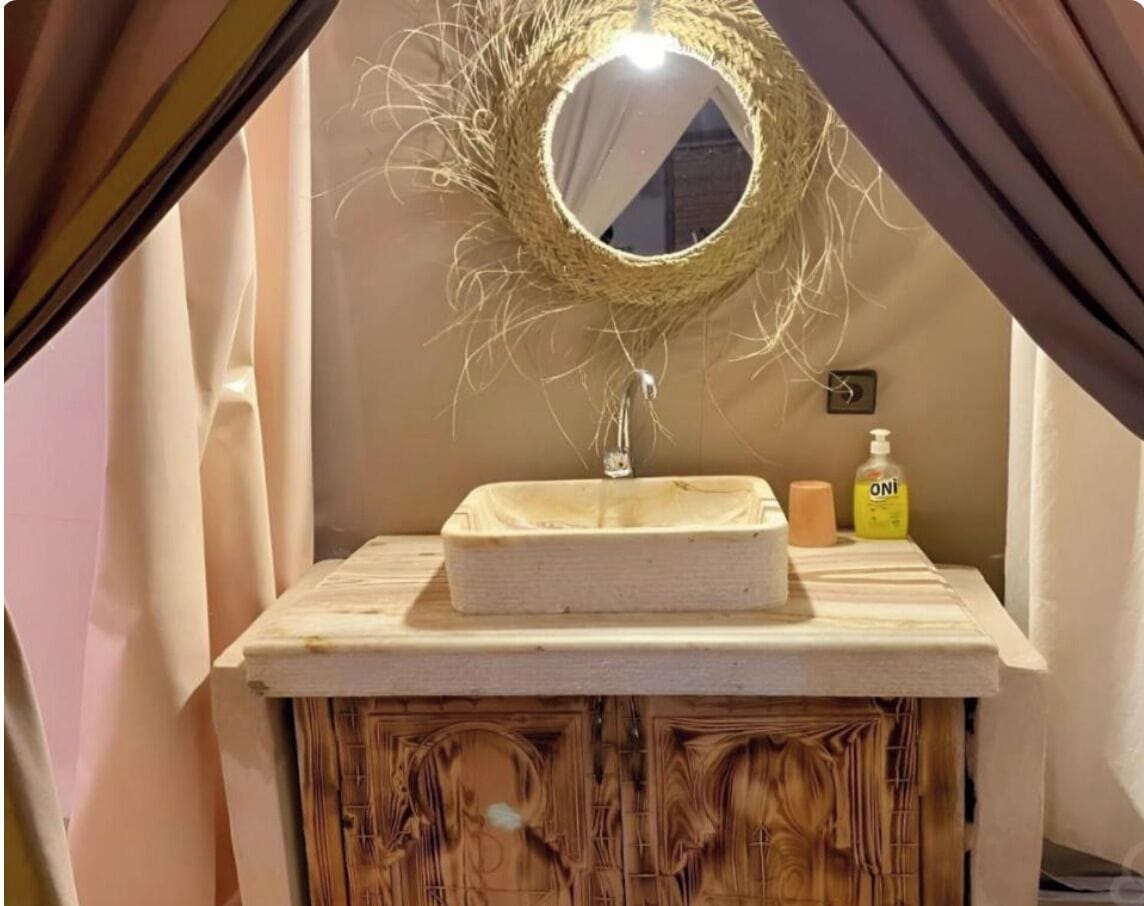 A bathroom with a wooden vanity, a round mirror with a woven frame, and a small sink.