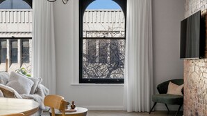 A modern living room with a large window, a brick wall, a green armchair, and a round table with a bowl. - Avenue Apartment 1 - luxe Suite -
Inner City - Free Parking (Launceston)