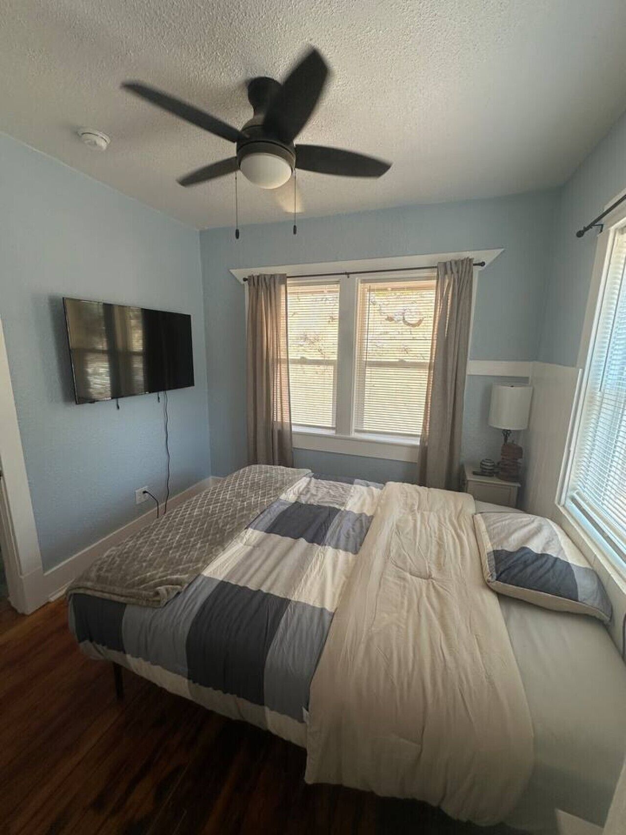 Quarto com cama, ventilador de teto, televisão e janela com cortinas.