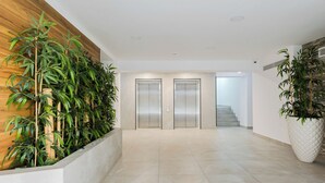 Een moderne hal met twee liften, een trap en een houten wand met groene planten.