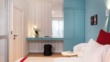 A modern bedroom with a bed, a bedside table, a small round table, a black stool, and a window with curtains.
