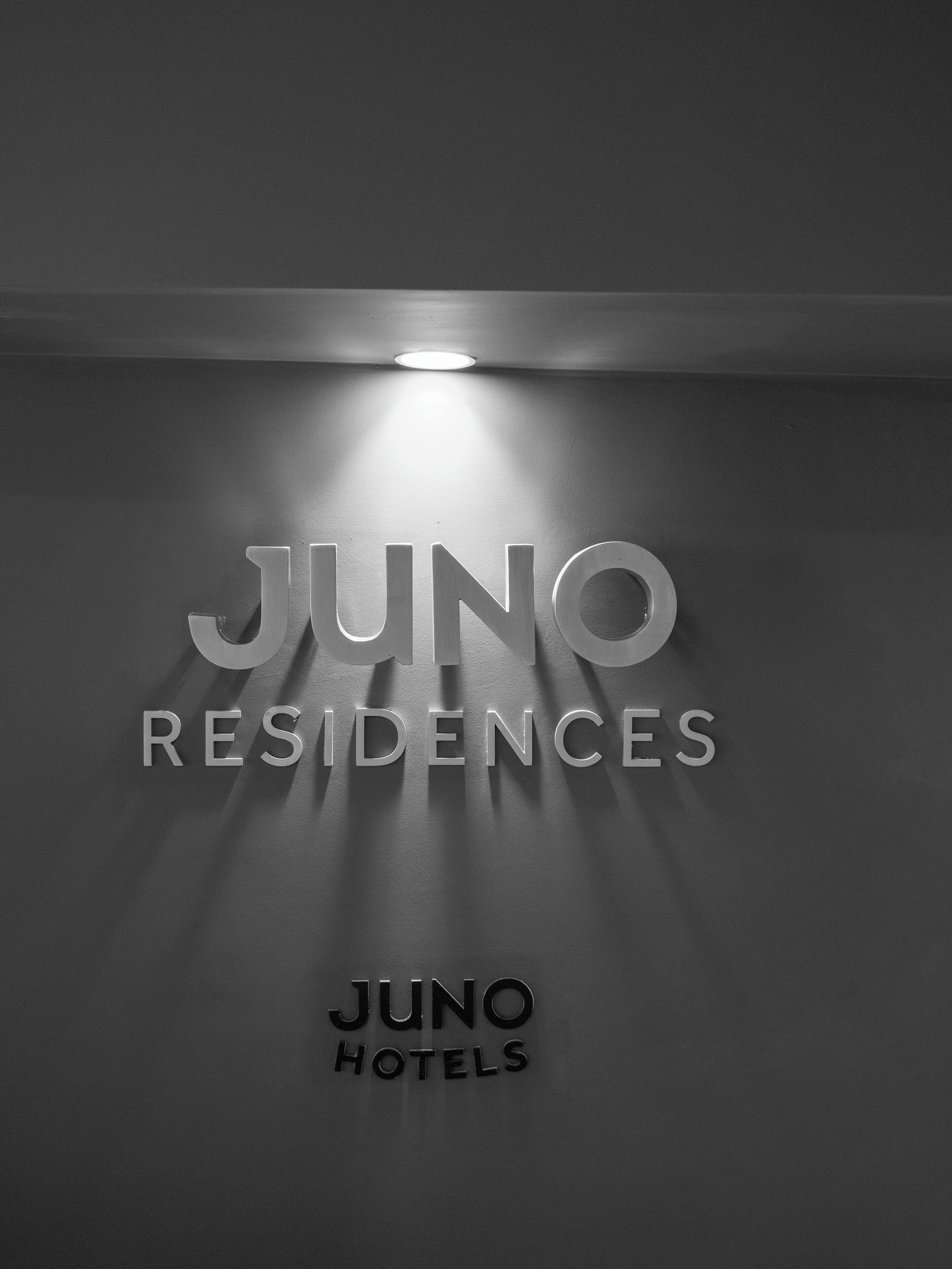 A wall with the text 'JUNO RESIDENCES' illuminated by a ceiling light.