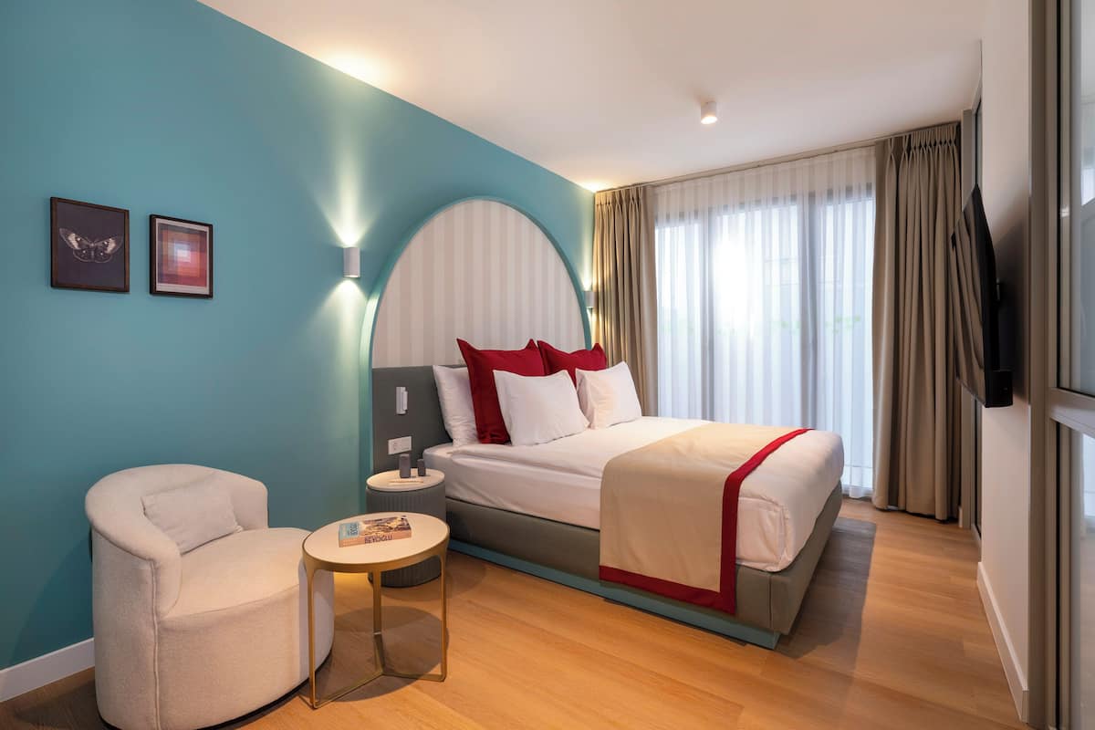 A hotel room with a bed, a chair, a small table, and a TV.