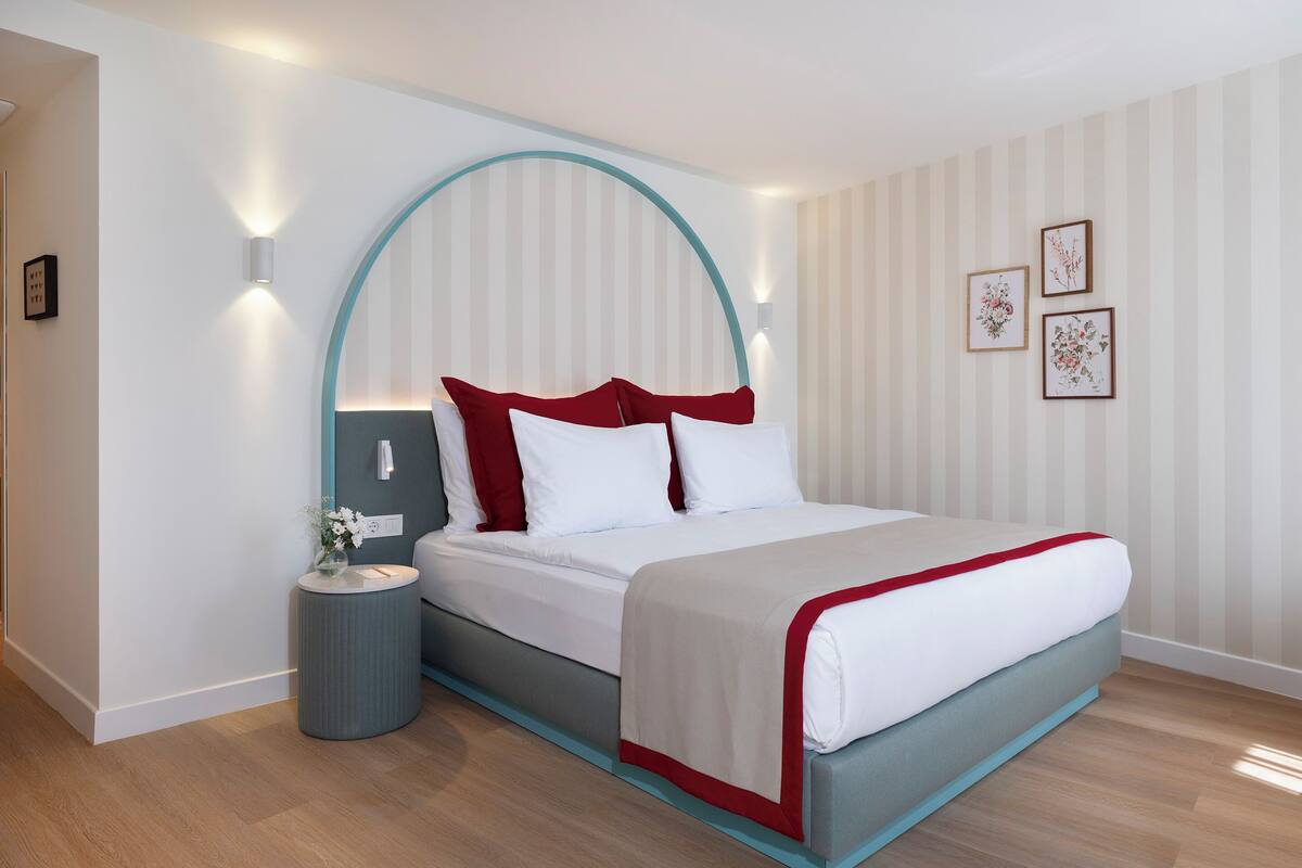 A modern hotel room with a bed, a bedside table, and a wall-mounted light fixture.