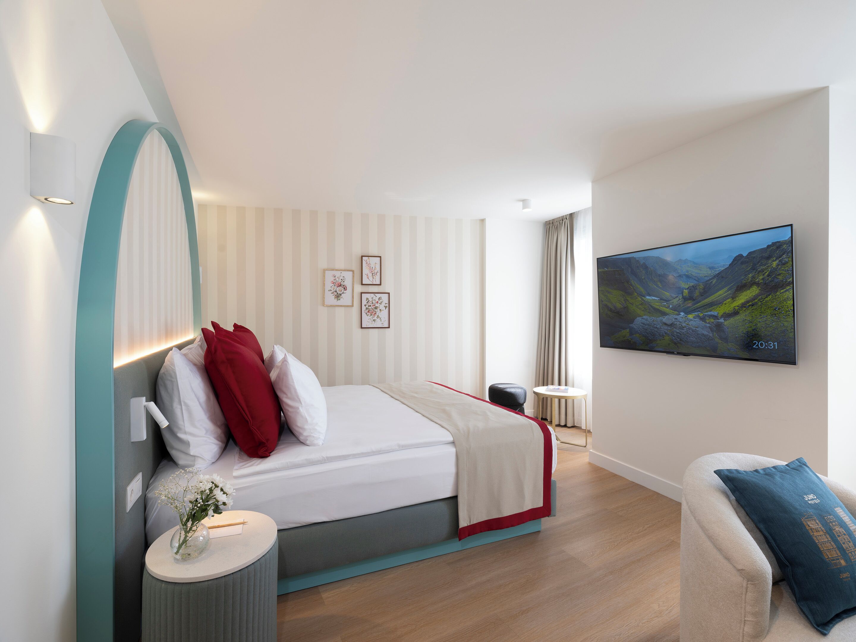 Una habitación de hotel moderna con una cama, una mesita con un florero, una silla y un televisor en la pared.