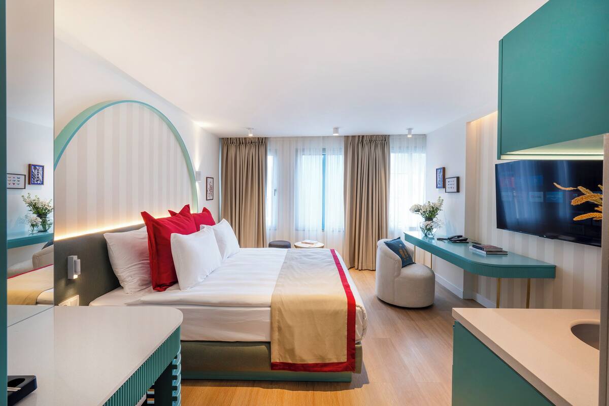 A modern hotel room with a large bed, a desk, a television, and a bathroom.