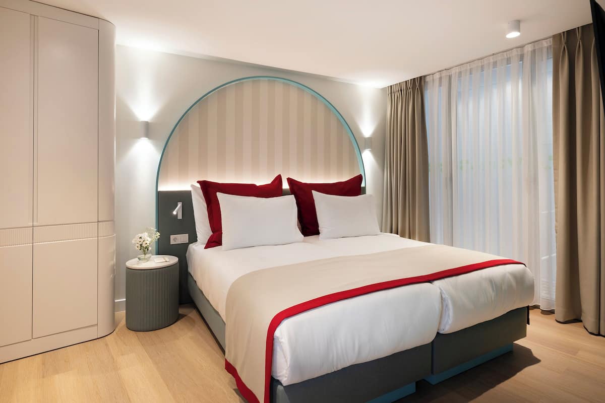 A modern hotel room with a large bed, a bedside table, a nightstand, and a curved wall design.
