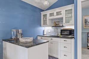 A kitchen with white cabinets, a marble countertop, a coffee machine, and a microwave.