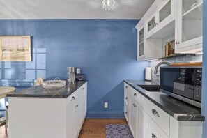 Une cuisine avec des meubles blancs, un plan de travail noir et un mur bleu.