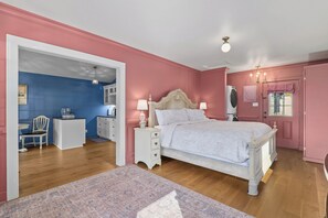 Ein Schlafzimmer mit Bett, Nachttischen, einem Schminktisch, einem Stuhl und einer Tür zu einem anderen Raum.