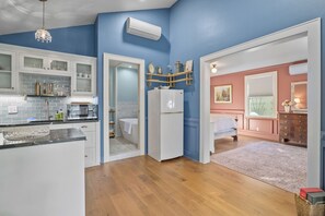 A modern kitchen with white cabinets, a built-in oven, and a sink. There is a hallway leading to a bedroom with a bed and a dresser.