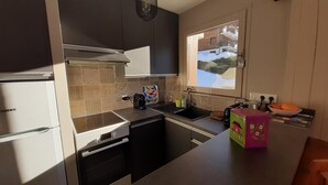 A compact kitchen with a built-in oven, a microwave, and a sink. There is a window with a view of a snowy landscape. - Wifi, 1st floor, balcony, parking, tv, ski locker, 44m², Le Grand Bornand (Le Grand-Bornand)