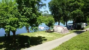 A camping area with a tent, a truck, and a path by a lake.